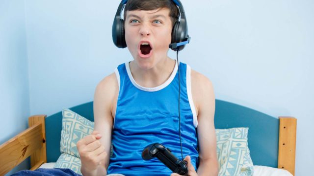 Foto: Shutterstock. Gutt med hodetelefoner og spillkonsoll er engasjert i et spill.