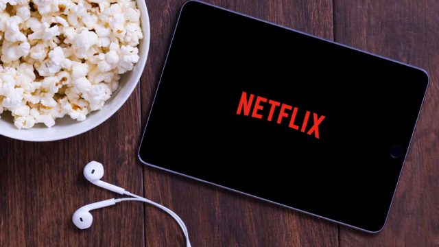 Foto: Shutterstock / Studio R3. Bildet viser et nettbrett med Netflix-logo. Ved siden av høretelefoner og en bolle med popcorn.
